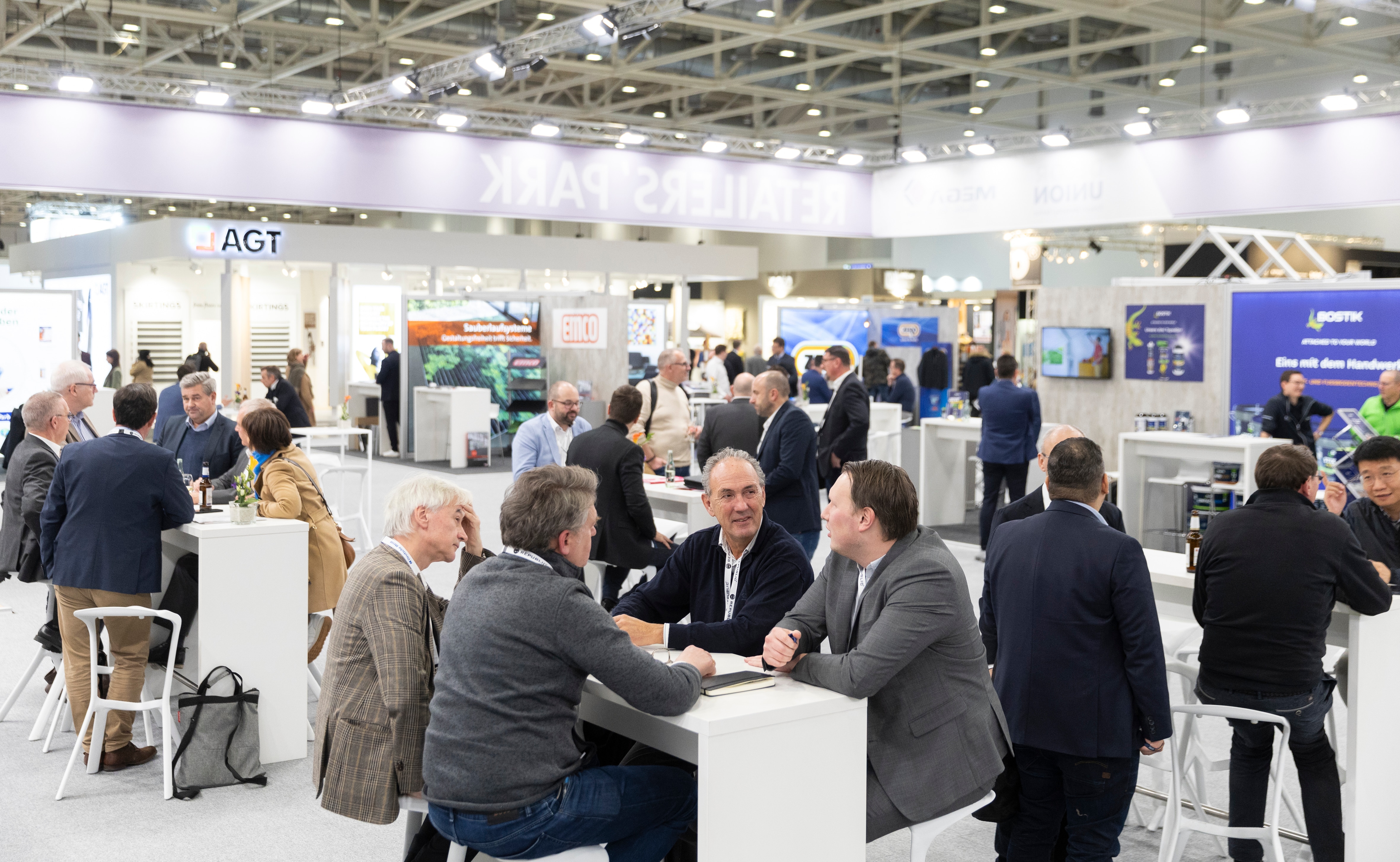 Visitors at the DOMOTEX trade fair stand and sit at high tables, talking and networking in the “Retailers Park” exhibition area.