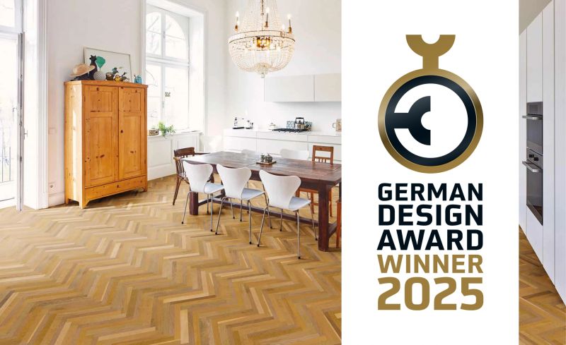Bright living and dining area with a wooden herringbone parquet floor. A dining table with chairs stands beneath a chandelier, next to a wooden cabinet. On the right, the “German Design Award Winner 2025” logo is displayed. The image presents award-winning flooring design in a classic, modern interior.