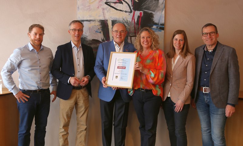 Group photo of an award ceremony: Several people stand next to each other and present a framed certificate. The picture documents the official recognition of a company for its commitment to environmental and sustainability management.